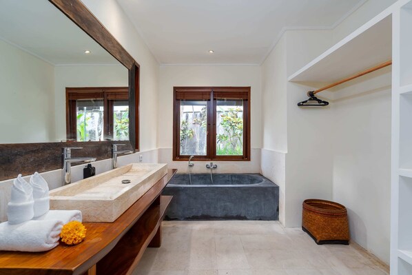 A modern bathroom with a large mirror, a bathtub, and a wooden vanity.