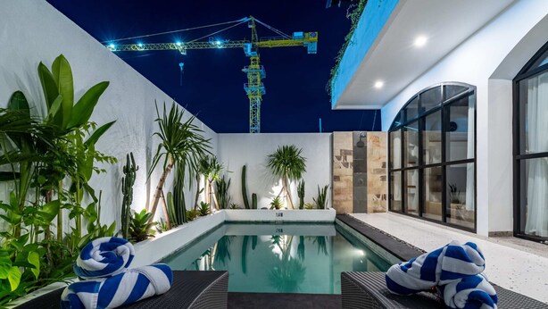 A modern indoor pool area with a clear view of the pool, surrounded by potted plants and a large window. - Villa Ambrogio A (Canggu)