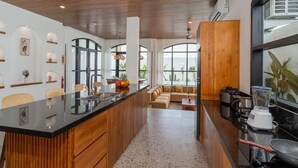 A modern kitchen with a central island, wooden cabinetry, and a large window providing natural light. - Villa Ambrogio A (Canggu)