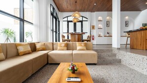 A modern hotel lobby with a large beige sectional sofa, a wooden coffee table with a scale, and a kitchen area in the background. - Villa Ambrogio B (Canggu)