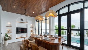 A modern kitchen with a central island, wooden ceiling, and large windows overlooking a pool. - Villa Ambrogio B (Canggu)