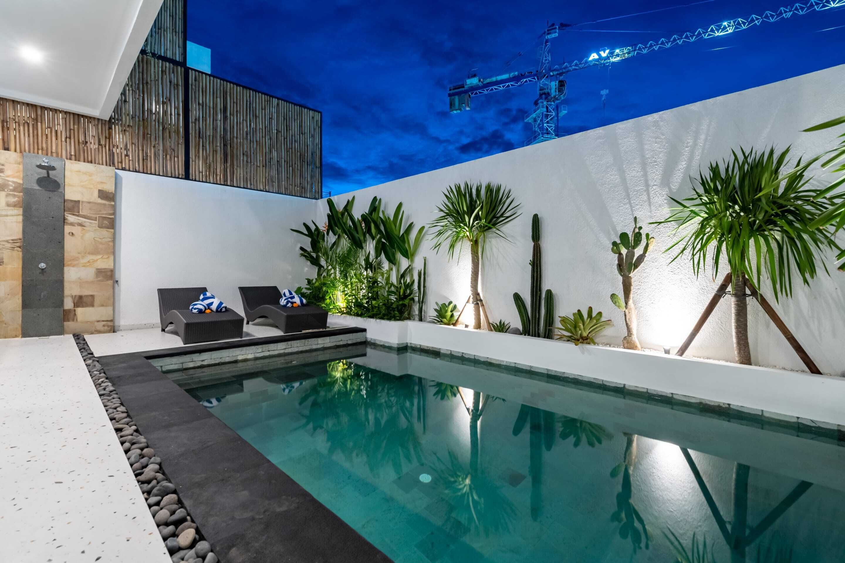 Un área de piscina interior moderna con una piscina cristalina, sillas de descanso y varias plantas.