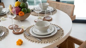 Una mesa redonda para comer con platos, tazones y cubiertos blancos.