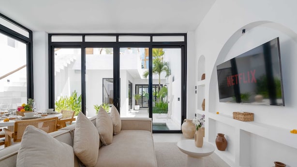 Una sala de estar moderna con sofá, televisor y comedor con mesa dispuesta para dos.