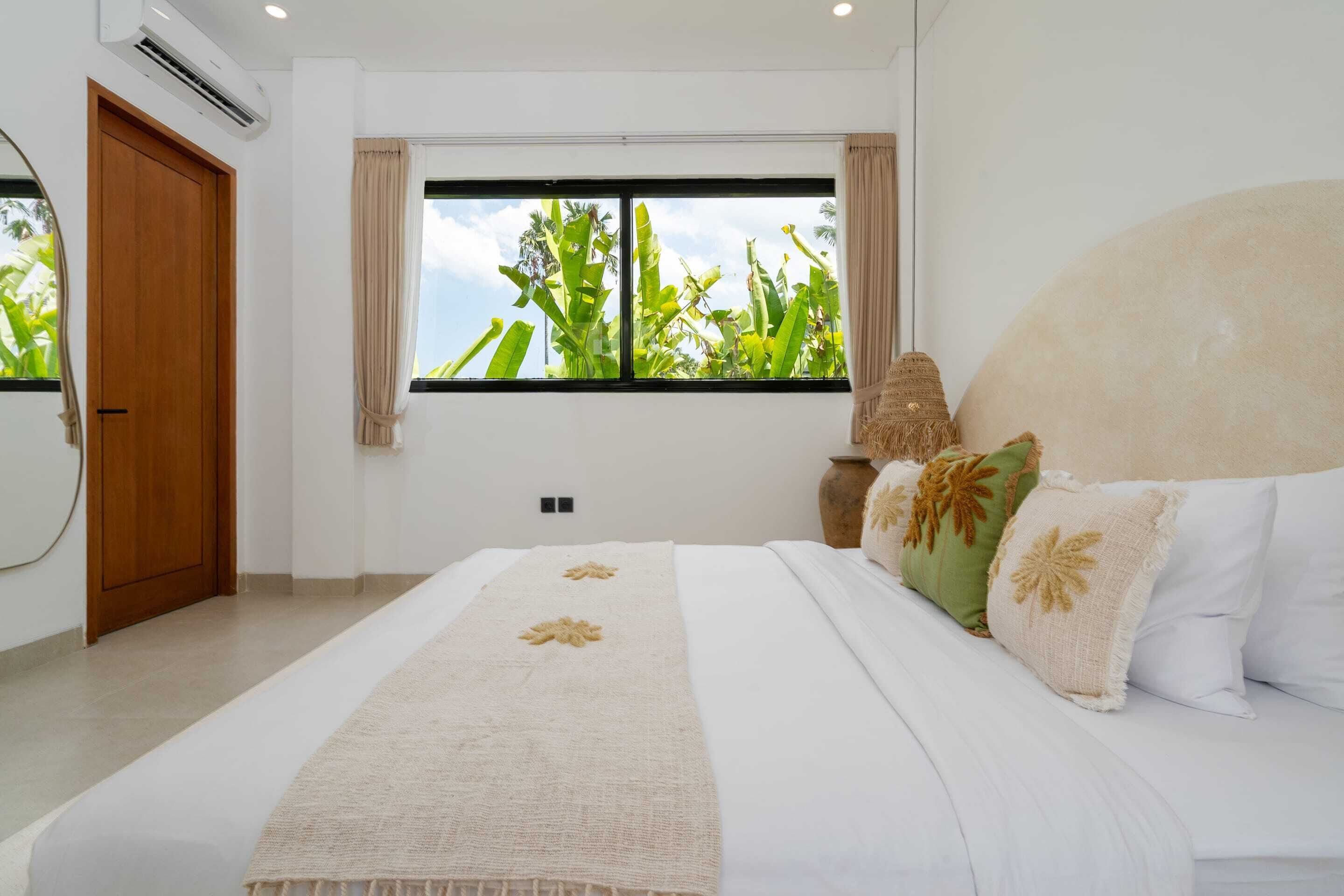 Une chambre avec un grand lit, une fenêtre donnant sur un paysage verdoyant, une porte en bois et un appareil de climatisation.
