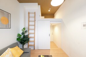 Un salon moderne avec un canapé, une plante et une échelle menant à une mezzanine.