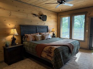 A bedroom with a large bed, two bedside tables with lamps, a ceiling fan, and a window with blinds.