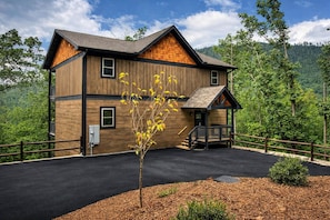 A two-story wooden cabin with a front porch, surrounded by a forested landscape. - Private Indoor Pool Cabin, Theater, Game Room, Hot Tub & Fire Pit (Gatlinburg)