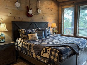 Quarto com cama, duas luminárias, um violão, um banjo e uma janela com persianas.
