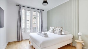 A modern bedroom with a large bed, a bedside table, a lamp, and a window with curtains.