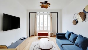 A modern living room with a flat-screen TV, a blue sofa, a wooden coffee table, and a unique ceiling light fixture.