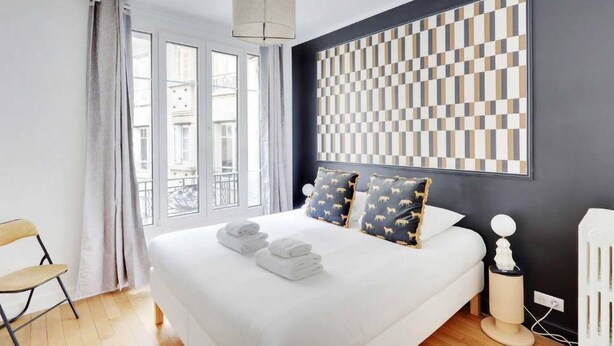 A modern hotel room with a large bed, a view of the city, and a checkered wall pattern.