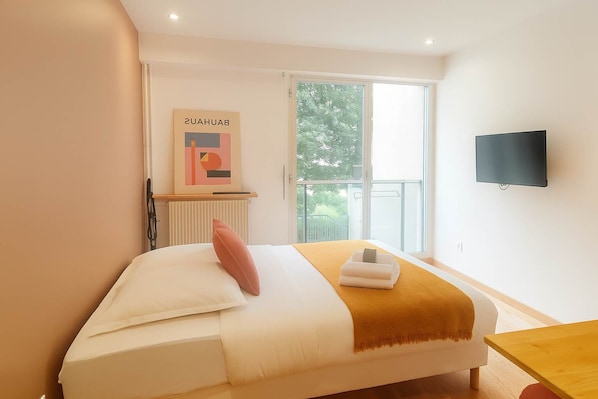 A bedroom with a bed, a window, a radiator, a television, and a framed picture on the wall.