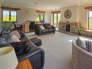 Ein großzügiges Wohnzimmer mit Kamin, Ledersofas, einem Essbereich und großen Fenstern mit Blick ins Freie.