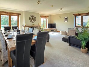 A dining area with a table set for six, a stone fireplace, a television, and a living area with a sofa and a plant. - 5 bedroom accommodation in Halfpenny, near Kendal (Halfpenny, near Kendal)