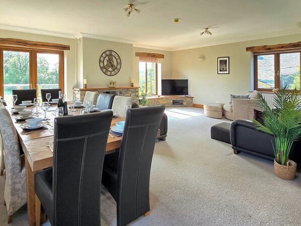 Un comedor con una mesa preparada para seis personas, una chimenea de piedra, un televisor y una sala de estar con un sofá y una planta.