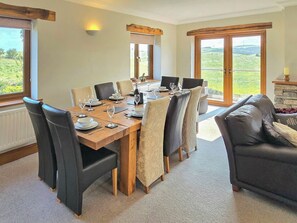 Comedor con una mesa de madera dispuesta para seis personas, rodeada de sillas, y vista a follaje a través de grandes ventanales.