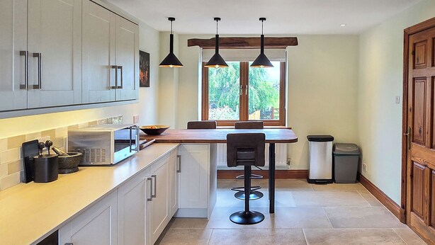 A modern kitchen with white cabinets, a wooden countertop, a bar stool, pendant lights, and a window with a view of greenery. - 5 bedroom accommodation in Halfpenny, near Kendal (Halfpenny, near Kendal)