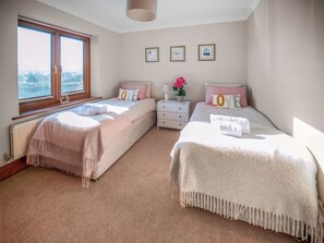 Ein Schlafzimmer mit zwei Betten, einem Fenster, einem Heizkörper, einem Nachttisch und gerahmten Bildern an der Wand.