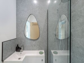 Un bany modern amb un mirall gran, una dutxa i un lavabo amb dosificador de sabó.