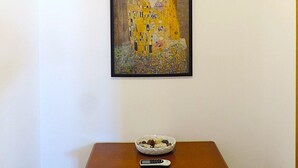 Un quadro incorniciato raffigura una donna con un abito giallo appeso a una parete, un tavolino con una ciotola e un telecomando, e un condizionatore d'aria sopra.