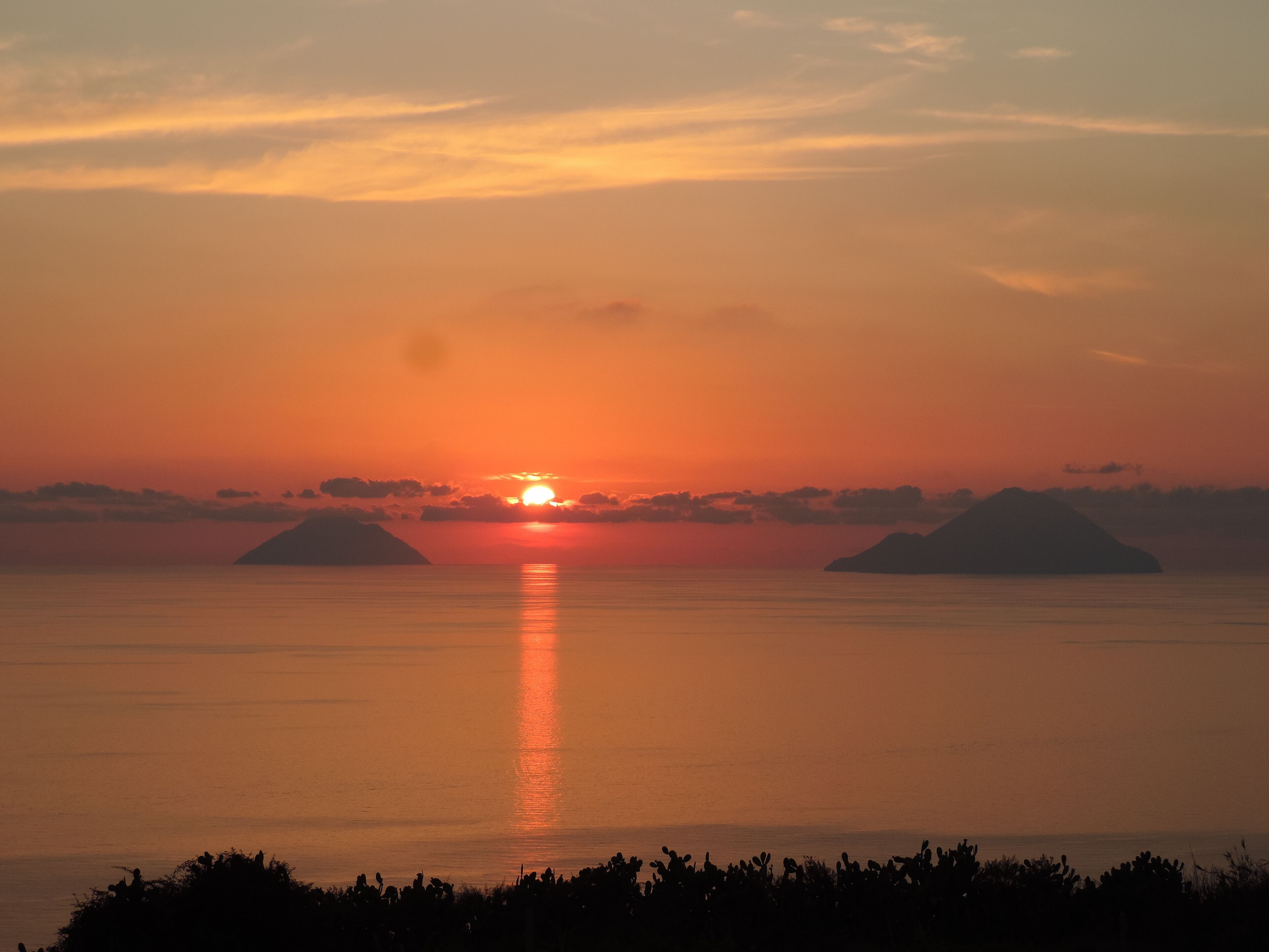 Un coucher de soleil sur des eaux calmes, avec deux îles se détachant en silhouette sur le ciel.