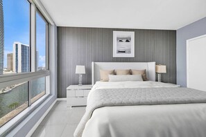 A modern hotel room with a large bed, a nightstand, a framed picture, and a view of the city.
