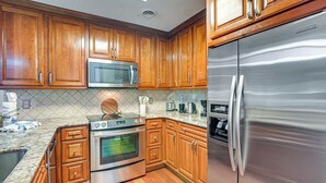 Cozinha com armários de madeira, eletrodomésticos de aço inoxidável, incluindo geladeira, micro-ondas e forno, e painel de azulejos.