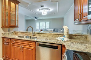 A kitchen with granite countertops, wooden cabinets, a stainless steel sink, and a dishwasher. - Steps to Sand: Walkable Condo in Myrtle Beach! (Myrtle Beach)