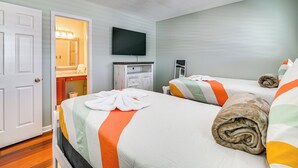 Quarto de hotel com duas camas, televisão, banheiro com espelho e luminária no teto.