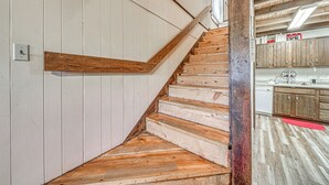 Eine Holztreppe mit weiß verkleideter Wand, die zu einem Küchenbereich mit Holzschränken und einem roten Teppich führt.