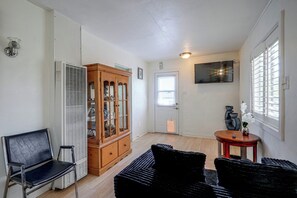 A room with a wooden cabinet, a black chair, a small table with a vase, and a television mounted on the wall. - Fullerton Home Base: Easy Access to Dtwn + CSUF! (Fullerton)