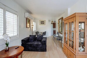 A living room with a black sofa, a wooden cabinet with glass doors, and a dining area with a table and chairs. - Fullerton Home Base: Easy Access to Dtwn + CSUF! (Fullerton)