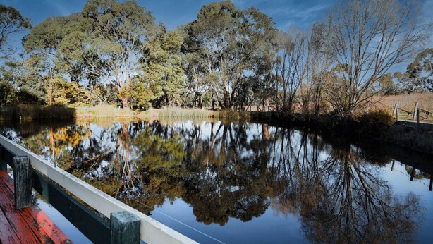 A calm river reflecting trees and a wooden bridge. - Gisborne Peak Winery - Cottages   • Vineyard Stay Macedon Ranges (Gisborne)