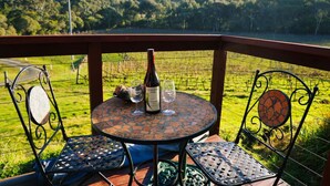 A round table with a wine bottle and glasses, surrounded by metal chairs with decorative backs, set on a balcony with a vineyard view. - Gisborne Peak Winery - Cottages • Vineyard Stay Macedon Ranges (Gisborne)