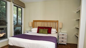 Camera da letto con un letto grande, una testata imbottita in legno, comodini e una finestra con vista sugli alberi.