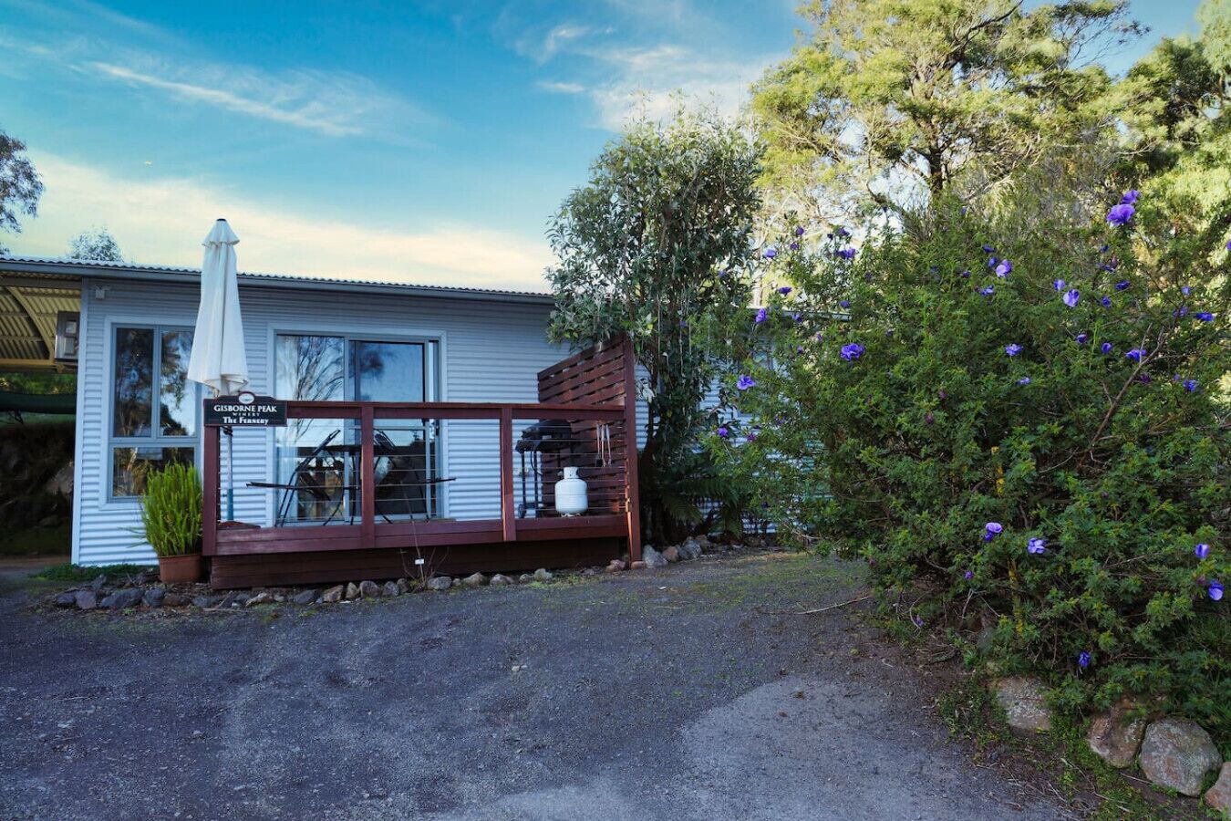 Una casa con porche, un letrero que dice "Gisborne Peak The Innery" y un arbusto con flores moradas.