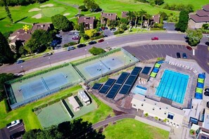 Vista aérea de una zona residencial con piscina, canchas de tenis y paneles solares.