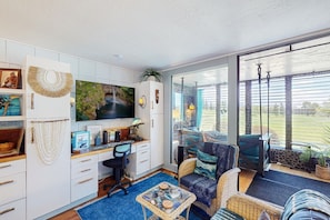 Una sala de estar moderna con un escritorio, un televisor grande y una zona de estar cómoda con vistas al exterior.