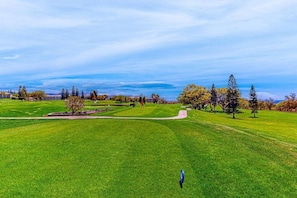 Un campo de golf con cielo despejado, césped verde, árboles y un edificio distante.