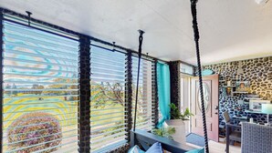 A room with a stone wall, a swing, a sofa with cushions, and a view of a garden. - Golfer’s Lava Cove - Waikoloa, HI (Waikoloa Village)