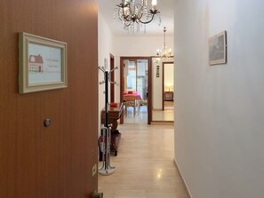 A hallway with a wooden door, a framed picture, a chandelier, and a dining area in the background.