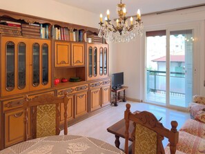 A room with a wooden cabinet, a television, a dining table with chairs, and a chandelier.