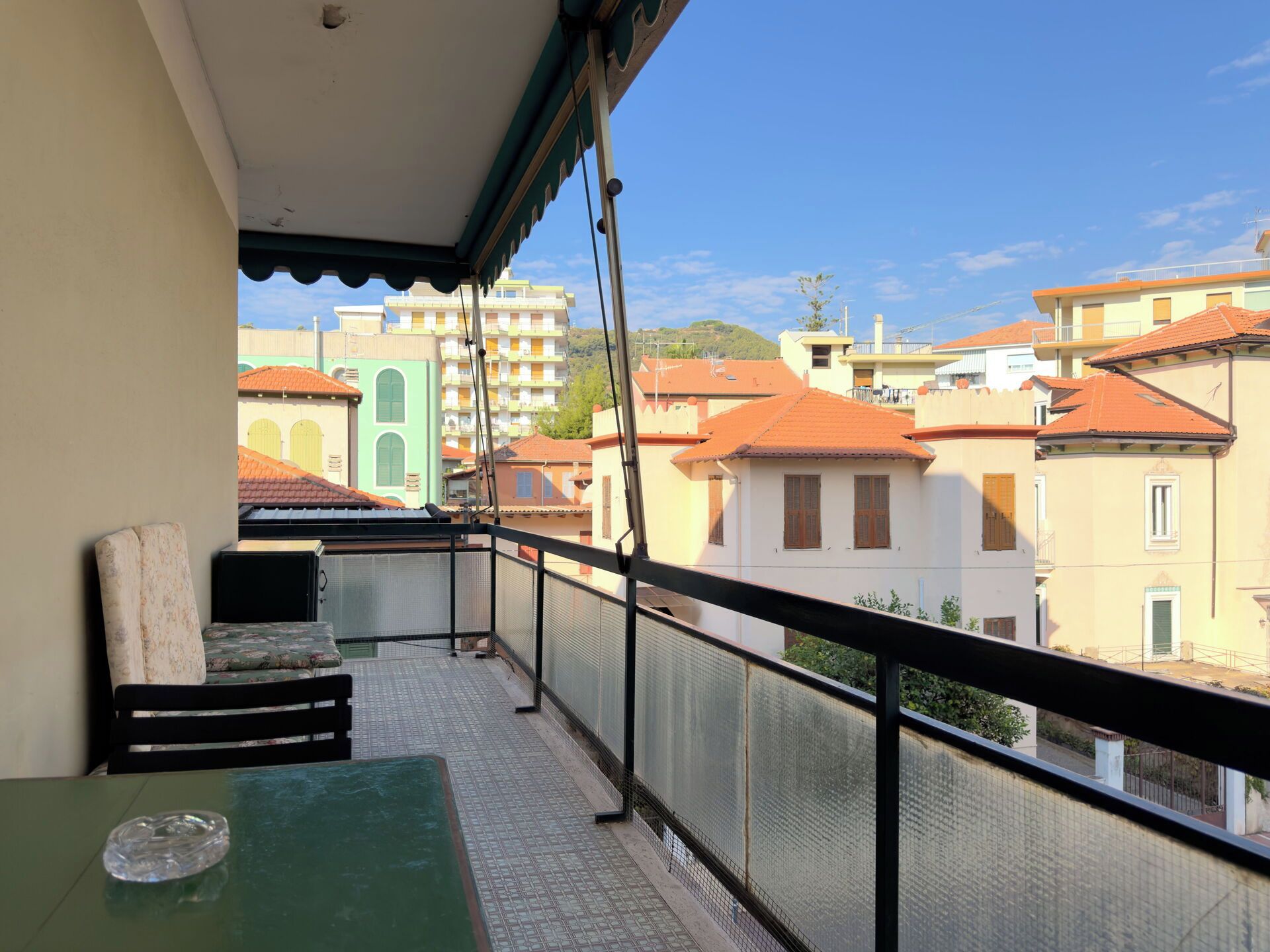 A balcony with a table and a chair, overlooking a residential area with buildings.