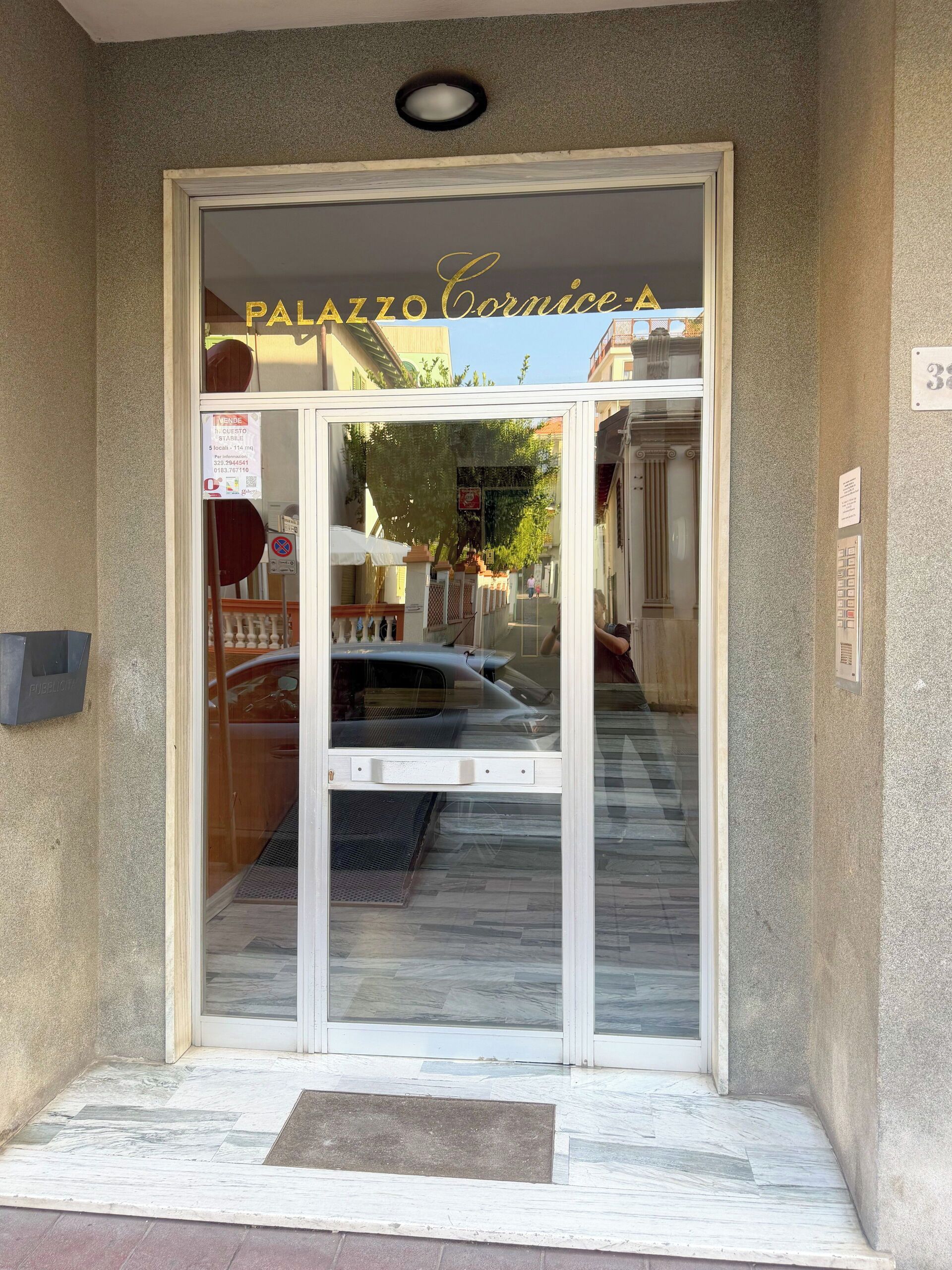 A hotel entrance with a glass door, a sign above the door, and a doormat.