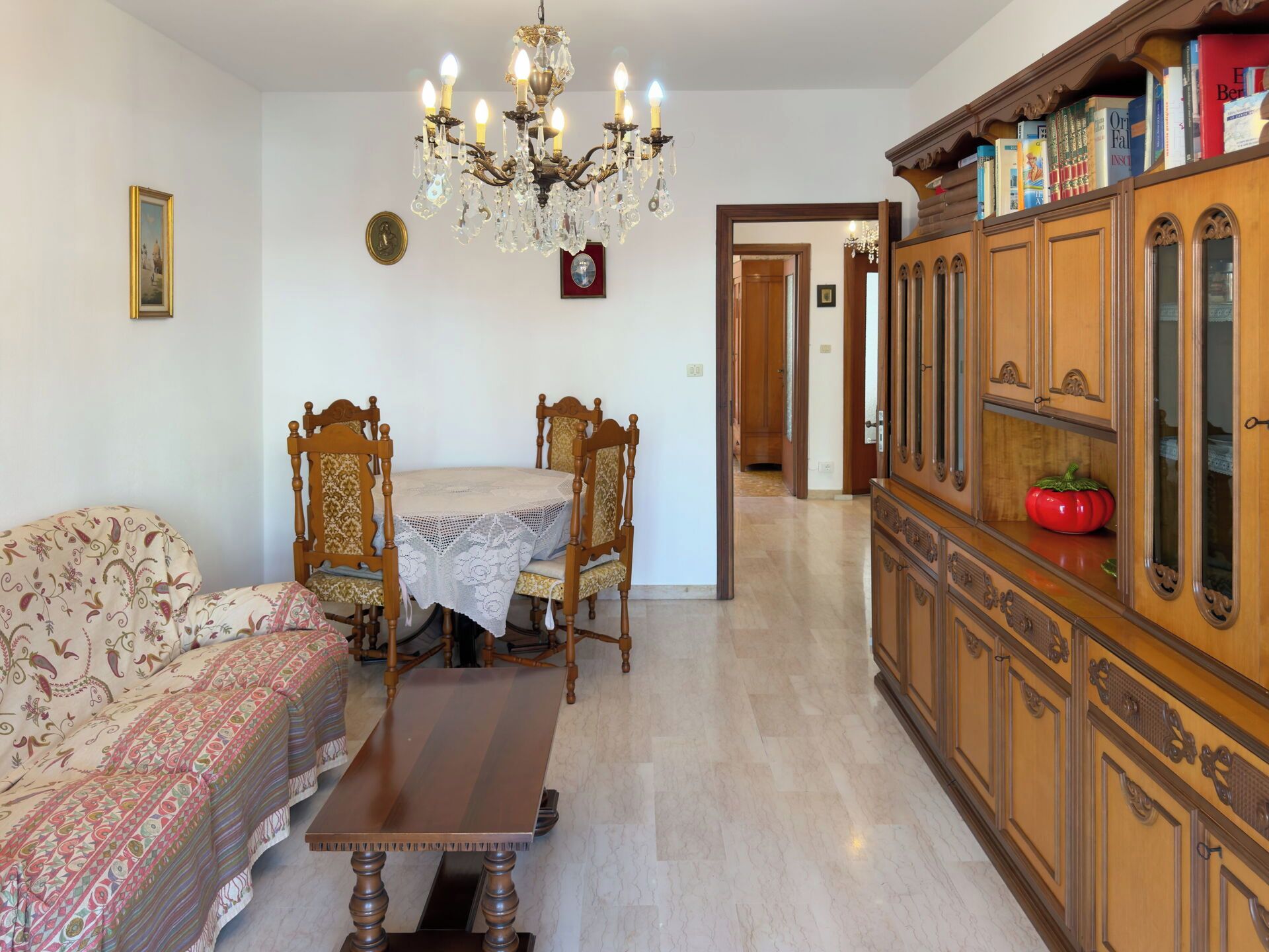 Une pièce comprenant une table à manger, des chaises, un canapé, un meuble en bois rempli de livres et un lustre.
