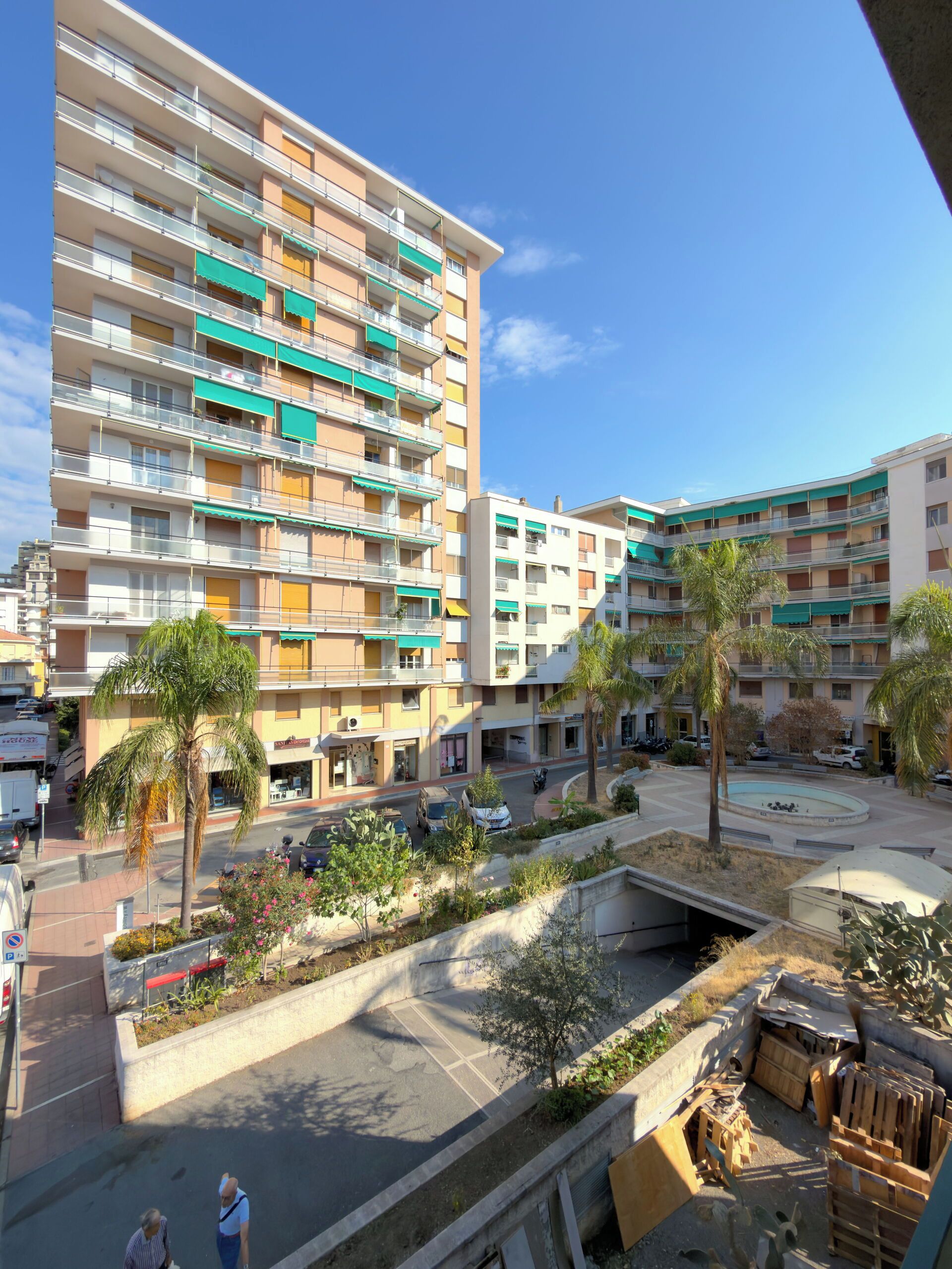 Un immeuble résidentiel à plusieurs étages, doté de balcons, d’une cour intérieure et entouré de végétation.