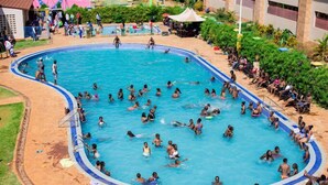 Una gran piscina al aire libre rodeada de una terraza de piedra, con gente nadando y relajándose.