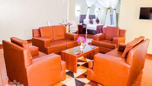 Un vestíbulo de hotel con sofás de cuero dispuestos alrededor de una mesa de centro, una cama con dosel al fondo y un televisor montado en la pared.