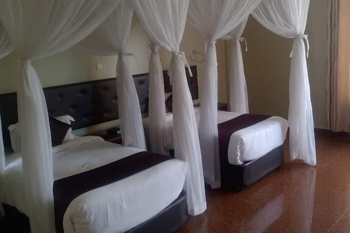 A hotel room with two beds, each with white bedding and a dark headboard. The room has a wooden floor and is decorated with white curtains.